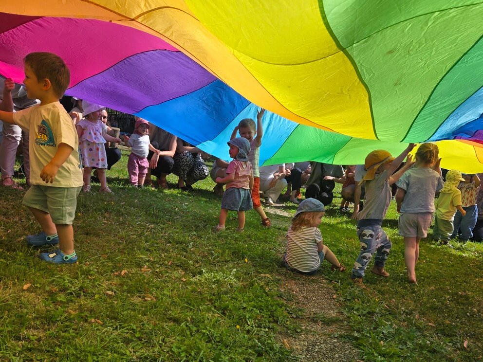 Kinder unter einem Regenbogenschwungtuch haben Freude